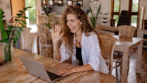 Imagem de uma mulher de longos cabelos cacheados sorrindo enquanto utiliza um notebook