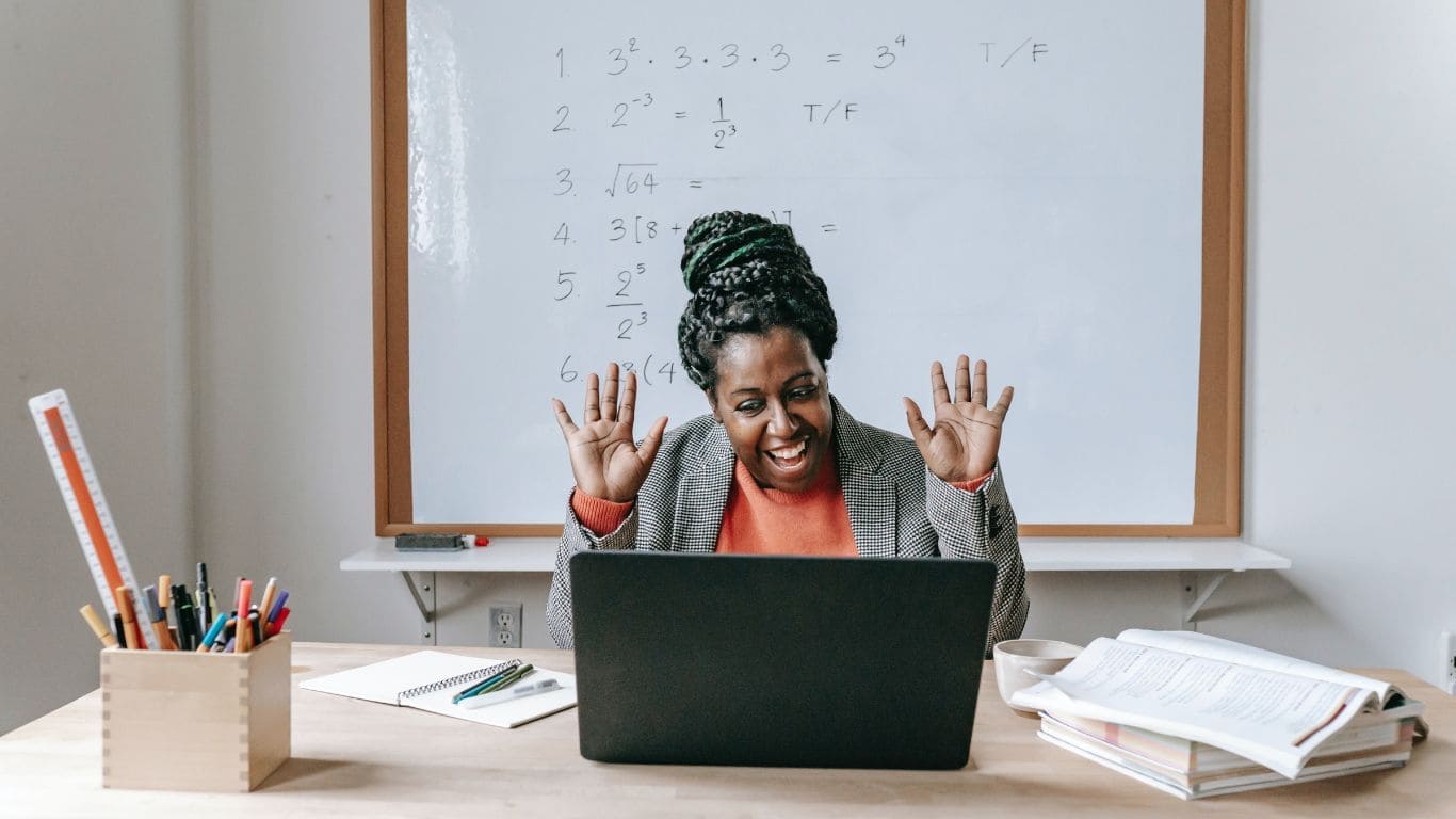 Imagem de uma mulher feliz utilizando um notebook e de costas para um quadro branco com anotações